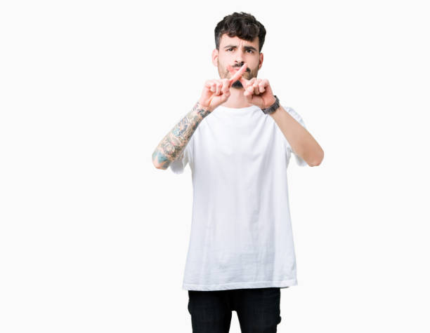 istock Young handsome man wearing white t-shirt over isolated background Rejection expression crossing fingers doing negative sign 1070964788