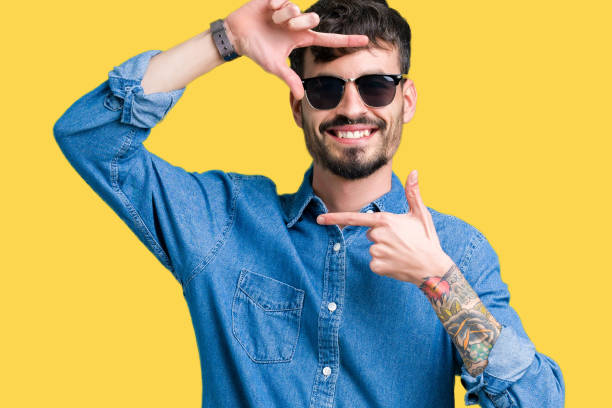 istock Young handsome man wearing sunglasses over isolated background smiling making frame with hands and fingers with happy face. Creativity and photography concept. 1070965302