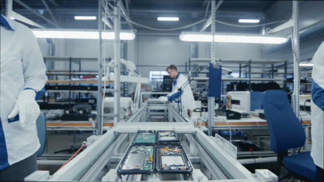 Time Lapse of Electronics Factory Workers Assembling Smartphone Circuit Boards by Hand While they Move on the Assembly Line. High Tech Factory Facility.