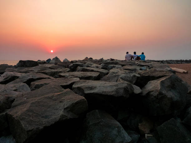 India, Kerala, Varkala, 02/19/2009: three men sit watching the sunset on the beach of Varkala
