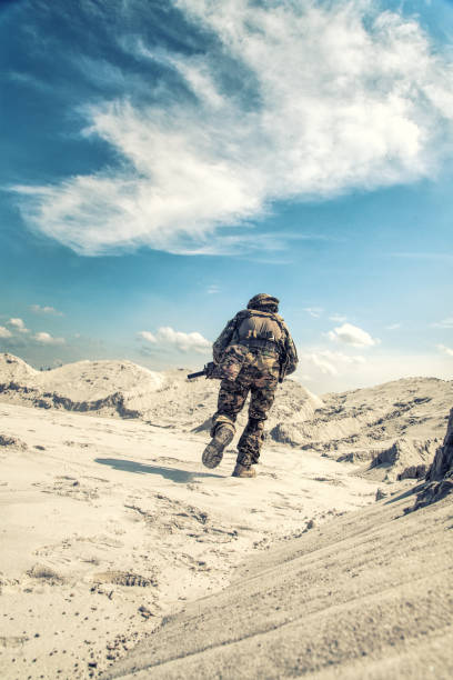 istock Man in military uniform playing airsoft in sands 1070971108