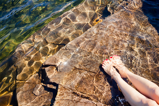 Young woman dipping her feet in a crystal clear water of a lake or fjord in Norway