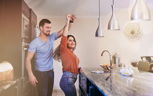 Shot of a young couple dancing in the kitchen at home
