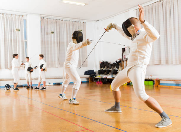 Adults and teens wearing fencing uniform practicing with foil Adults and teens wearing a fencing uniform practicing with foil at gym fencing sport stock pictures, royalty-free photos & images