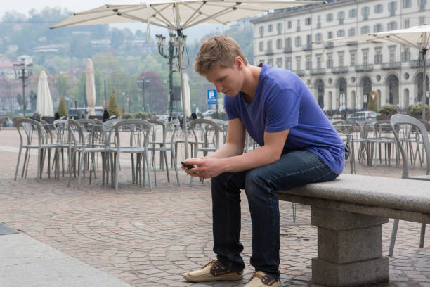 Young man uses cell phone while sitting in piazza on bench