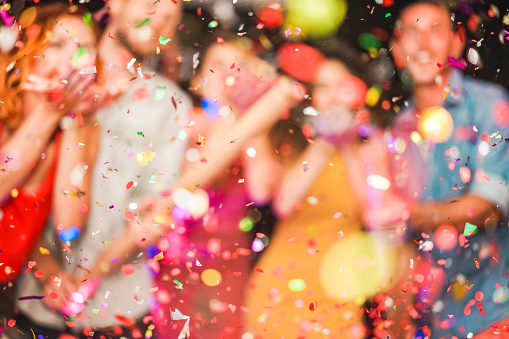 Blurred people making party throwing confetti - Young people celebrating on weekend night - Entertainment, fun, new year's eve, nightlife and fest concept - Defocused photo