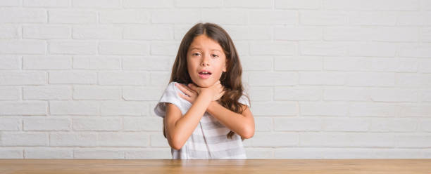 Young hispanic kid sitting on the table at home shouting and suffocate because painful strangle. Health problem. Asphyxiate and suicide concept. Young hispanic kid sitting on the table at home shouting and suffocate because painful strangle. Health problem. Asphyxiate and suicide concept. choking stock pictures, royalty-free photos & images