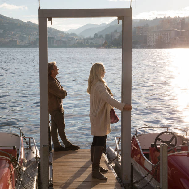 istock Couple stand on dock on lake with sun and mountains 1071000440