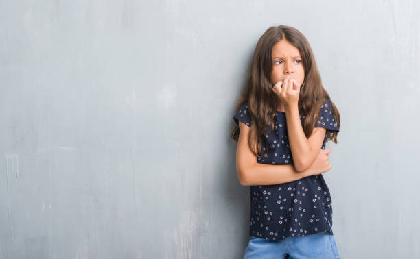 giovane ragazzo ispanico sopra la parete grigia grunge che sembra stressato e nervoso con le mani sulla bocca che morde le unghie. problema d'ansia. - preoccupato foto e immagini stock