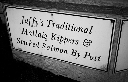 Sign outside a shop on Station Road in the village of Mallaig on the west coast of Scotland. It is an award winning speciality seafood shop, noted for its oat sherry wood treatment of its kippers. The village itself is famously located on the end of the Harry Potter railway line from Fort William, it serves as a ferry terminal to the south side of the Isle of Skye.