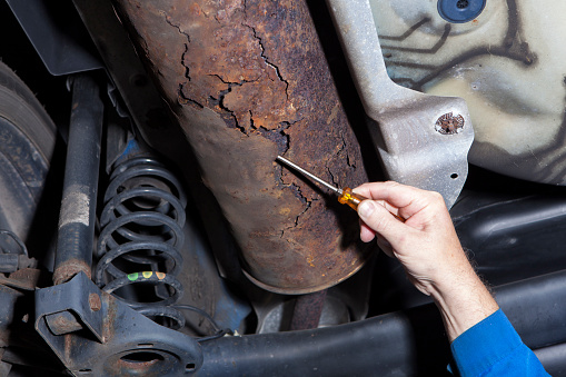 Auto repair shop, mechanic examines a rusted exhaust pipe