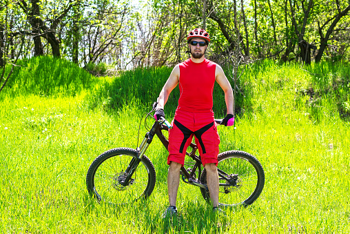 Man cyclist on nature in high grass, free space. A man in a bicycle helmet near a bicycle, an active lifestyle.
