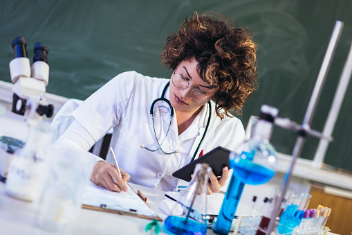 Portrait of confident female scientist working on digital tablet in chemical laboratory