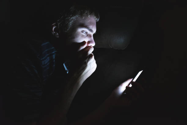 Shocked teenager on his cellphone in the dark. stock photo