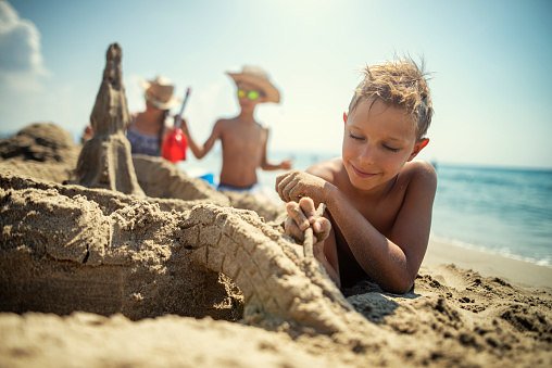 Happy smiling boy and sister girl play with sand, water at the ocean beach during summer vacations