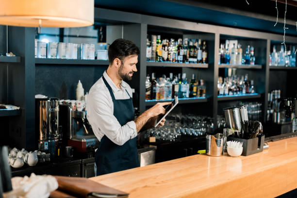 istock Barman standing in apron and typing on digital tablet 1071027230