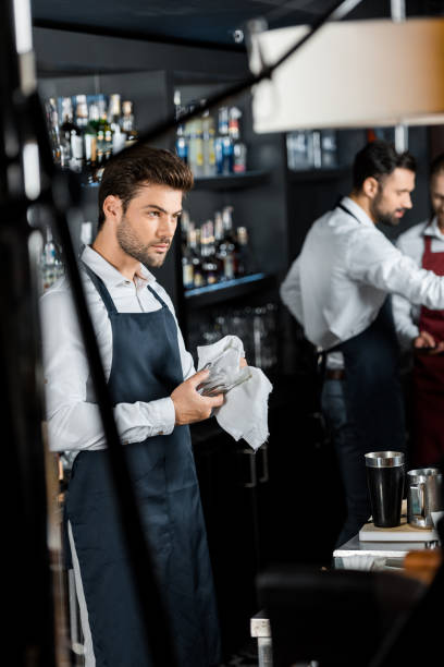 istock handsome barman rubbing up glass with cloth at workplace 1071027268