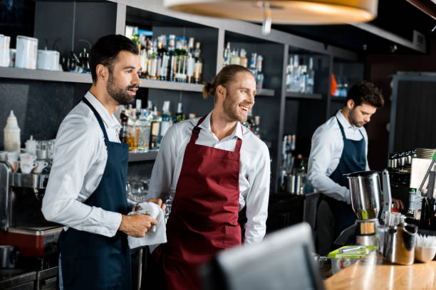 istock handsome cheerful barmen in aprons standing at workplace 1071027314