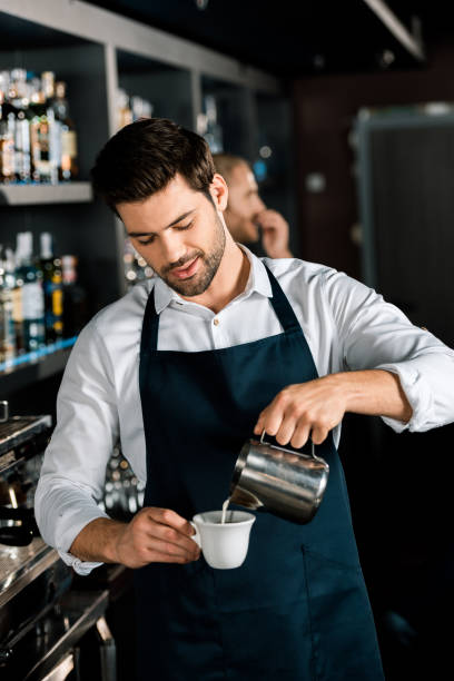 istock handsome barista in apron pouring milk from jar at workplace 1071027344