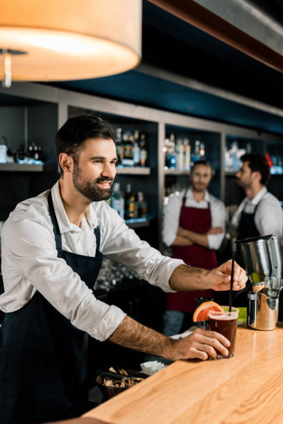 istock cheerful bartender putting straw in cocktail at wooden counter 1071027452