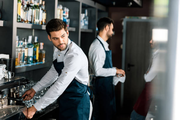 istock adult handsome barista in apron using coffee machine at workplace 1071027484