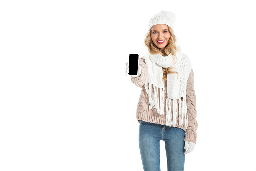 beautiful smiling woman in winter outfit showing smartphone with blank screen isolated on white
