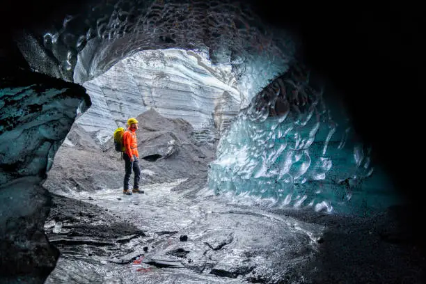 Hiker exploring ice cave in Kotlujokull. Male is standing in glacier. He is in Iceland during winter.