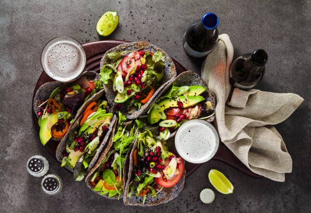 Gluten-free vegan tacos from black bean  with tomato and avocado salad  with tahini sauce and pomegranate seeds. healthy fast food for the whole family or party on a dark background with beer