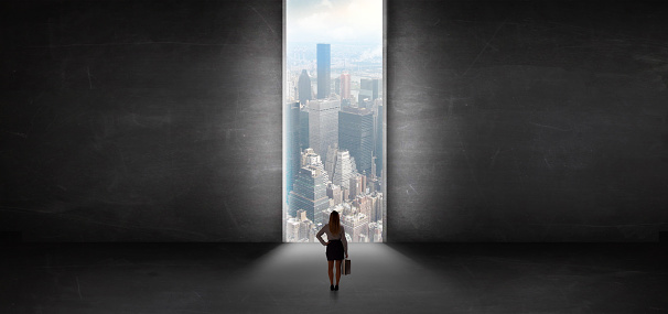 Woman standing in a dark room and looking outside to a cityscape view