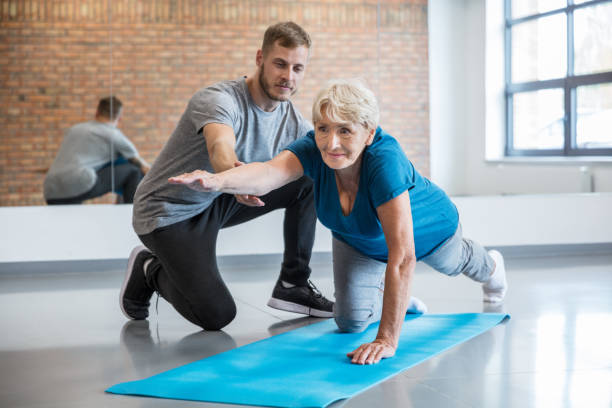 Senior woman exercising with trainer at rehab Senior woman being helped by her trainer in doing yoga workout at gym. Old woman with personal coach at rehab centre. physical therapy stretching stock pictures, royalty-free photos & images