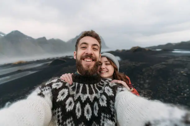 Photo of Woman and man making selfie near  Vestrahorn mountains near the sea