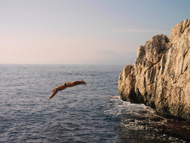 hombre se zambulle desde acantilado en mar - salto desde acantilado fotografías e imágenes de stock