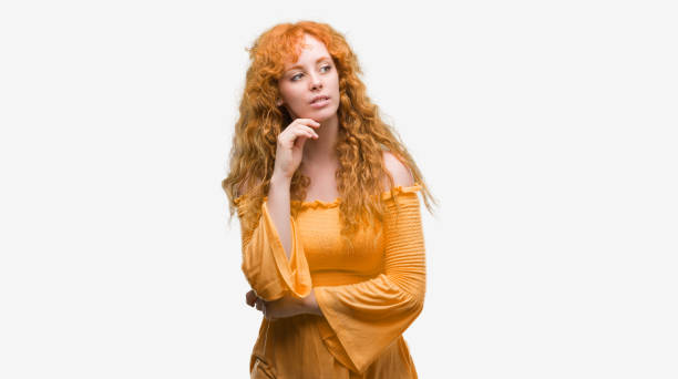 istock Young redhead woman with hand on chin thinking about question, pensive expression. Smiling with thoughtful face. Doubt concept. 1071093384