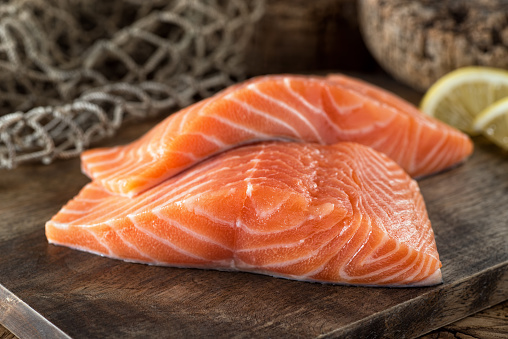 Fresh raw salmon fillets on a wooden board with lemon and fish net background.