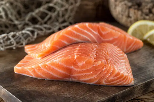 Fresh raw salmon fillets on a wooden board with lemon and fish net background.