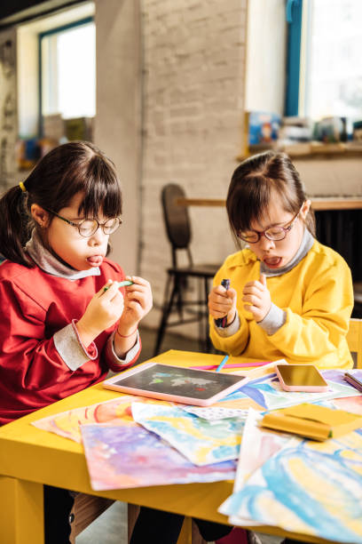 istock Two twins with Down syndrome sitting at yellow table and drawing 1071097286