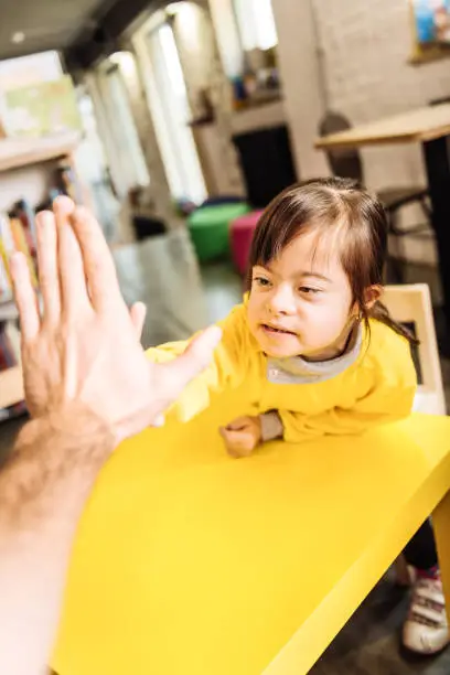 Five to father. Dark-eyed pleasant cute girl with Down syndrome giving high five to her father