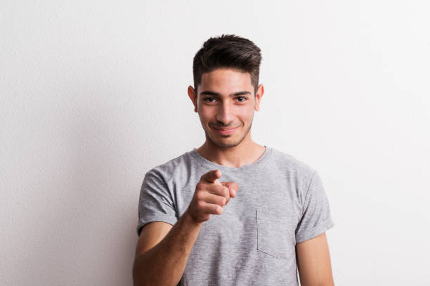 A portrait of cheerful young hispanic man in a studio, pointing a finger at a camera.