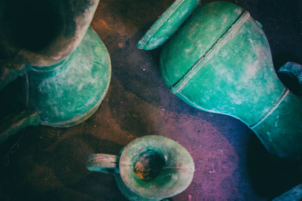 Wallpaper background of old vintage worn green ceramic water vases on the floor near a window with day light from the outside. No people.