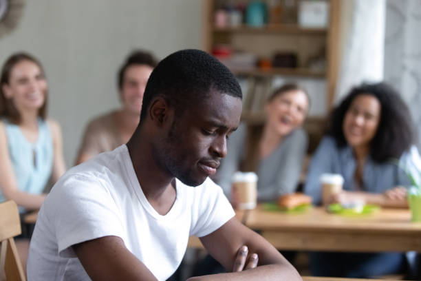 istock Upset black man sitting alone schoolmates scoffing him 1071116594
