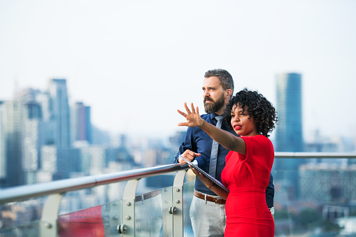 A portrait of businesspeople standing against London rooftop view, leaning on a railing and talking.