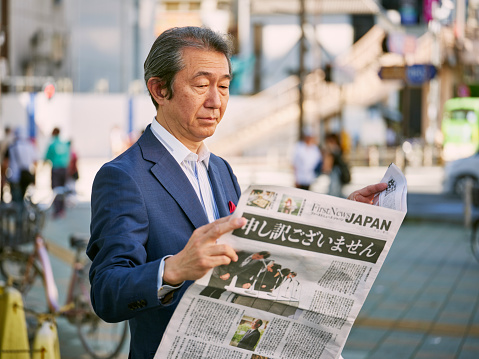 A Japanese businessman reading a newspaper on a city street in Tokyo, Japan.