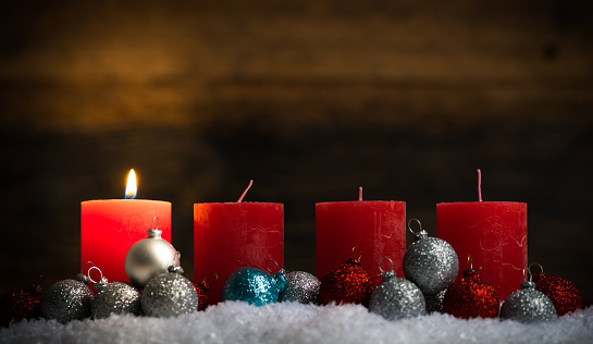 christmas balls and one of four lit candles in the snow in front of wooden background