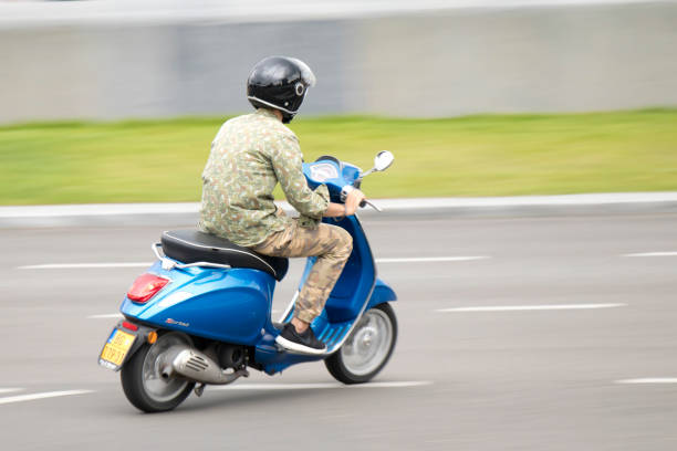 One young man in camouflage clothes riding fast blue scooter on empty city street stock photo
