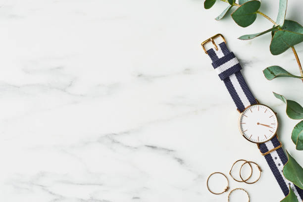 Women's watch with navy blue and white nylon strap Women's watch with navy blue and white nylon strap, golden rings and eucalyptus on white marble background. Top view with copy space for text. strap photos stock pictures, royalty-free photos & images