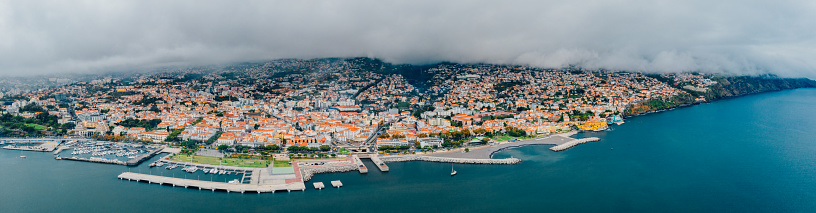 Aerial view of the Funchal old town - the capital of Madeira island during cloudy weather. Small houses with orange rooftops by the Atlantic ocean.