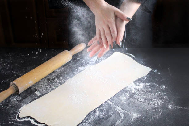 istock Woman hands clapping and sprinkling white flour over dough on kitchen background. Making dough by hands at bakery. Cooking Process Of Apple Roses. Step four prepare the dough for baking 1071177896
