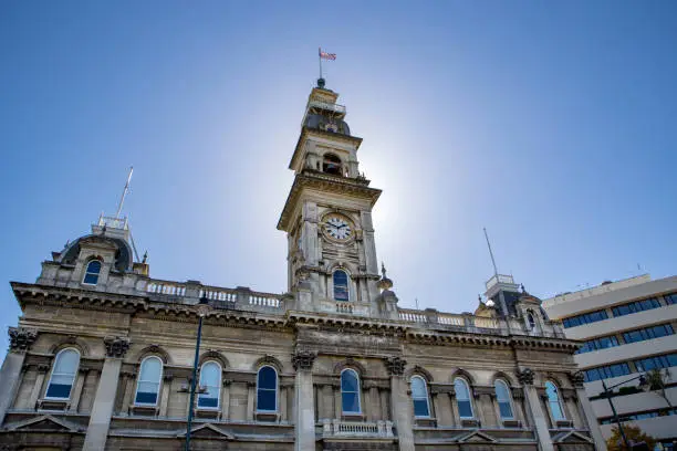 The clock tower on an old stone heritage building in the city of Dunedin is lit up in the sunlight
