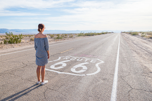 Young woman standing on an endless straight empty road in the middle of nowhere on the Route 66 road. Backpackers, visionary, entrepreneur, adventure concepts.