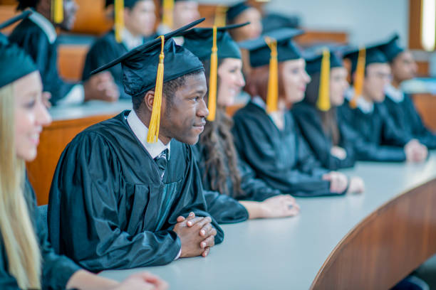 University students in academic robes and mortar boards attend a graduation ceremony inside an auditorium